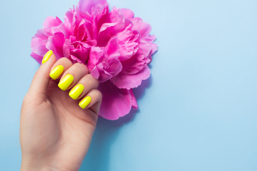 a hand with yellow nails and pink flowers